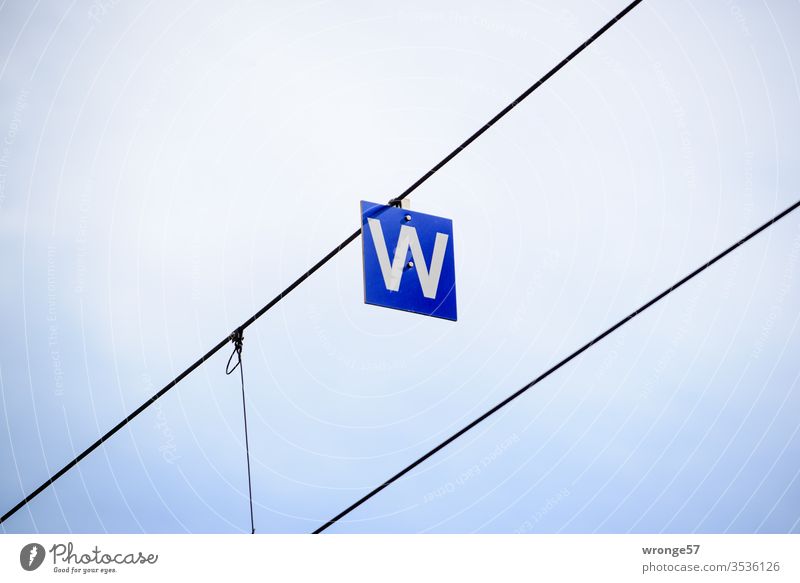 Ein weißes W auf blauer Tafel hängend an einem Drahtseil Buchstabe Schild Schilder & Markierungen Außenaufnahme Menschenleer Farbfoto Schriftzeichen Buchstaben
