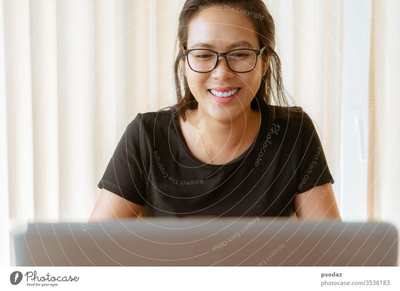 glückliche Frau mit Laptop. Junge asiatische Frau sitzt zu Hause und arbeitet am Laptop attraktiv offen lässig heiter Kaffeehaus Computer Tagung lockig