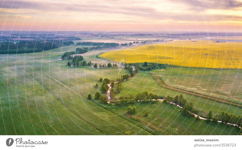 Ländliches Panorama am Frühlingsmorgen aus der Luft. Sonnenaufgang über grün und gelb blühenden Rapsfeldern Feld Morgen Fluss Nebel Bäume Wolken Antenne Erdöl