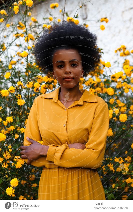 junge afroamerikanische Frau in gelbem Kleid, die sich an einem Garten mit gelben Blumen erfreut schwarze Frau Mädchen Menschen genießend Porträt Lifestyle cool
