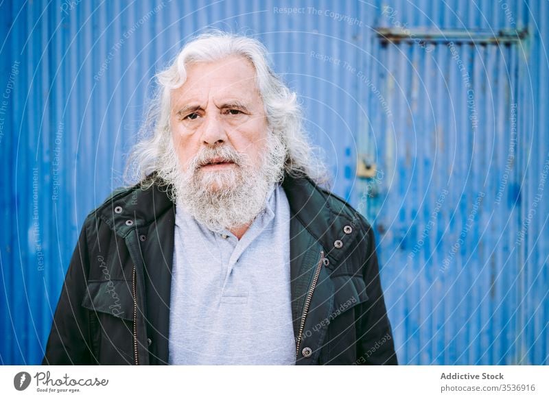Verschrumpelter alter Mann schlägt mit der Handfläche gegen die blaue Wand Hautfalten Garage Lifestyle Signet besinnlich älter schäbig Senior gealtert