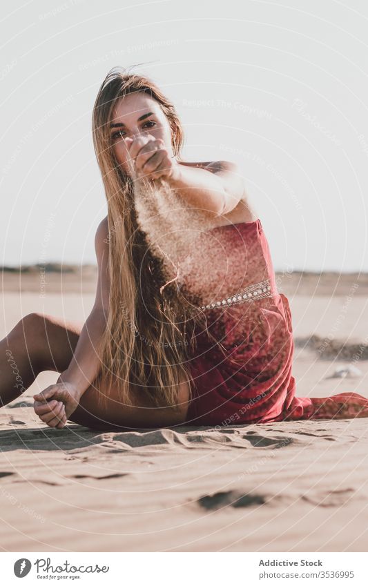 Stilvolle junge Dame sitzt am Strand und schüttet Sand durch die Finger Frau träumen eingießen sinnlich Sommer allein Küste Freiheit charmant blond attraktiv