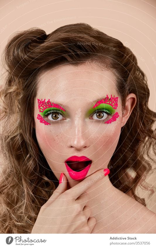 Erstaunte Frau mit leuchtendem Make-up farbenfroh erstaunt Konzept Stil Kinn reiben Mund geöffnet Model jung Vorschein Erstaunen Überraschung hell lebhaft