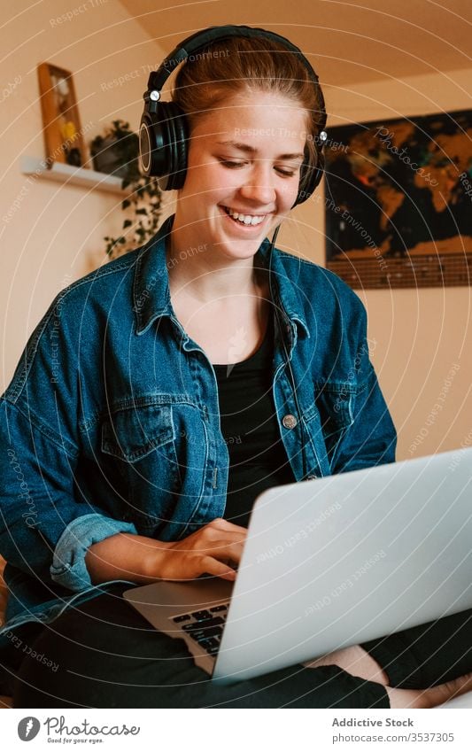 Fröhliche junge Frau mit Laptop im hellen Schlafzimmer zu Hause Kopfhörer heimwärts benutzend Bett lesen Surfen soziale Netzwerke zuschauen sich[Akk] entspannen