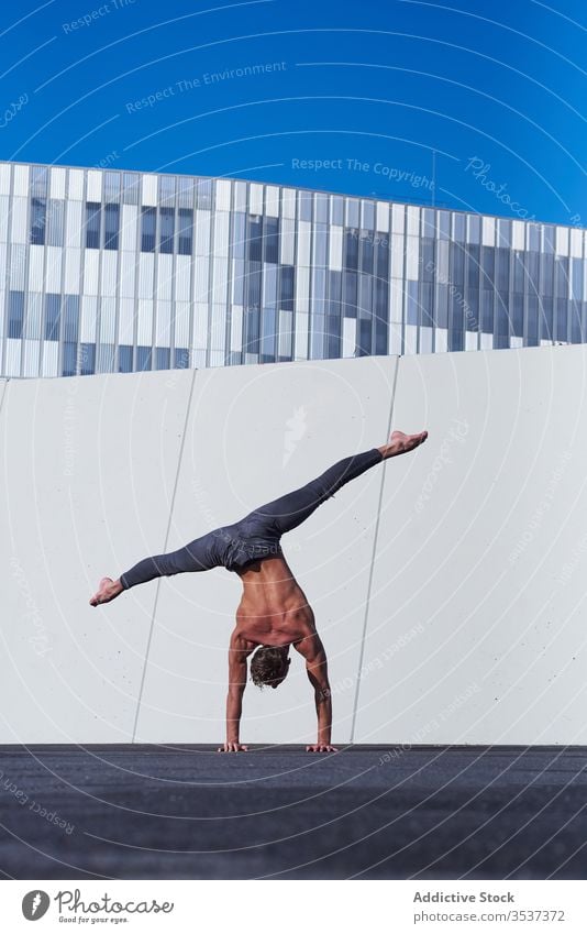 Männlicher Akrobat beim Handstand auf dem Dach Artist ohne Hemd Mann urban auf den Kopf gestellt entfernt Übung Dehnung Gleichgewicht muskulös ausführen stark
