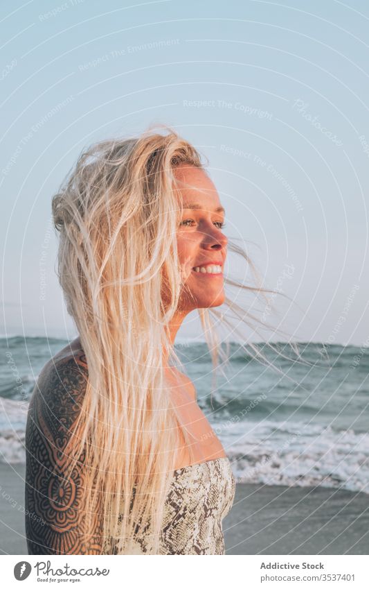 Lächelnde junge Blondine ruht sich bei Sonnenschein am Meeresufer aus Frau Strand Schulter Tattoo blond Sommer Sand Urlaub sich[Akk] entspannen Küste Natur Ufer