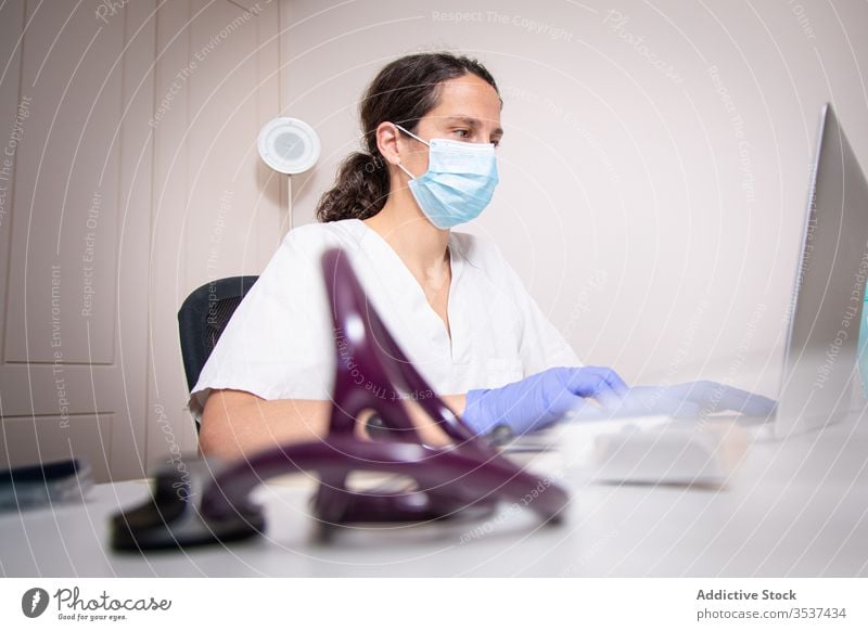 Junge Ärztin mit medizinischer Maske arbeitet am Laptop in der Klinik Frau Arzt Uniform Mundschutz Handschuh Schreibtisch ernst Krankenhaus professionell