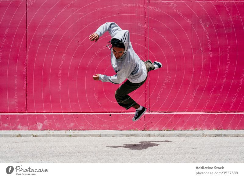 Junge hispanische Männer springen in der Nähe einer rosa Mauer auf die Straße urban Tanzen Lifestyle Großstadt posierend Stehen farbenfroh Tageslicht gemischt