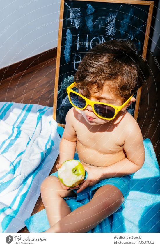 Glücklicher kleiner Junge mit Sonnenbrille, der zu Hause am Strand sitzt und vom Sommer träumt heimwärts Selbstisolierung Spaß träumen soziale Distanzierung