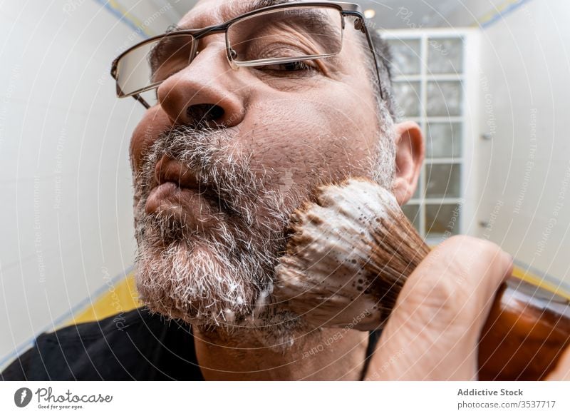 Mann trägt Rasierschaum mit Pinsel auf Rasieren schäumen Bürste bewerben vorbereiten Vollbart reif Bad Verfahren Hygiene Pflege männlich Lebensmitte Routine