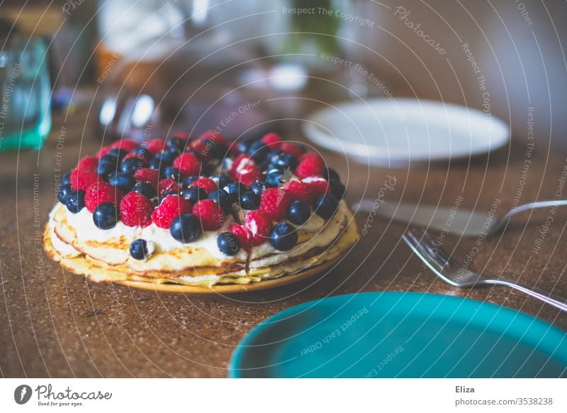 Eine Torte oder ein Kuchen mit Himbeeren und Heidelbeeren auf einem gedeckten Tisch Kuchenstück Kuchen essen Minze dekorieren Sahne liebevoll lecker Beeren
