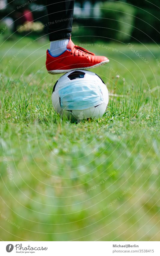 Fuß und Schuh mit Fußballfußball mit Gesichtsmaske für den Sport während der Pandemie covid-19 Konzept Korona COVID19 Gefahr Seuche Feld Spiel Gras Gesundheit