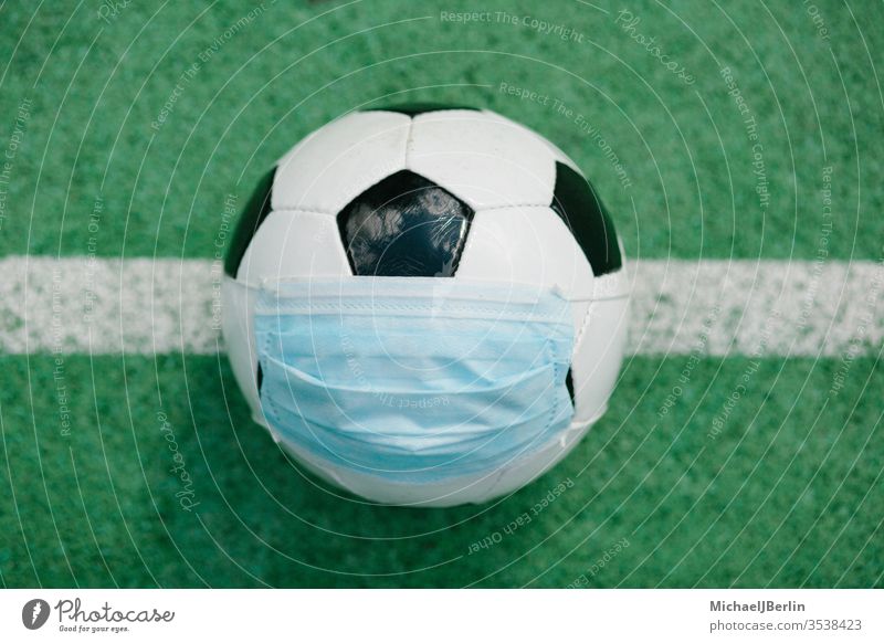 Fussball mit Gesichtsmaske für den Sport während der Covid-19-Pandemie Fußball künstlich Konzept Korona covid-19 COVID19 Gefahr Seuche Feld Spiel Gras grün