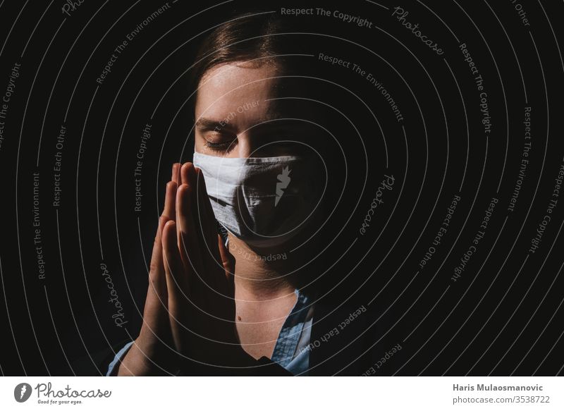 Religiöse Frau mit Maske, die mit Händen dafür betet, dass Coronavirus covid-19 auf schwarzem Hintergrund endet Erwachsener schwarzer Hintergrund Kaukasier