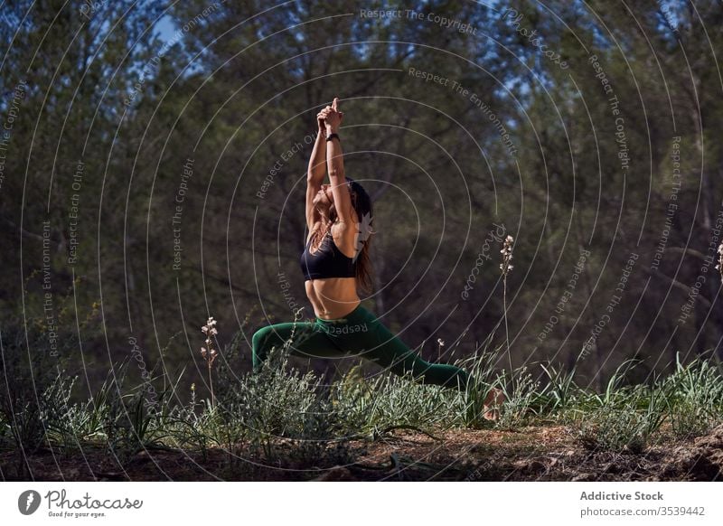 Ganzkörper einer konzentrierten Sportlerin in aktiver Kleidung, die tagsüber in der Natur Yoga praktiziert Konzentration üben Asana Sonne passen Krieger-Pose