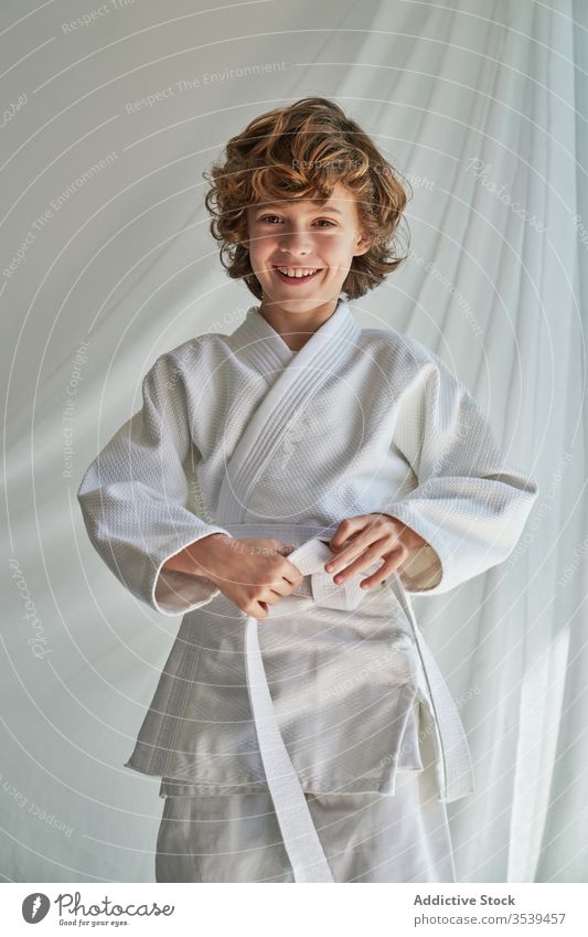 Positiver Junge in weißem Kimono, der zu Hause Judo übt Training Gurt kämpferisch Kunst Atelier Bestimmen Sie Lächeln selbstbewusst Sport positiv jung Kindheit