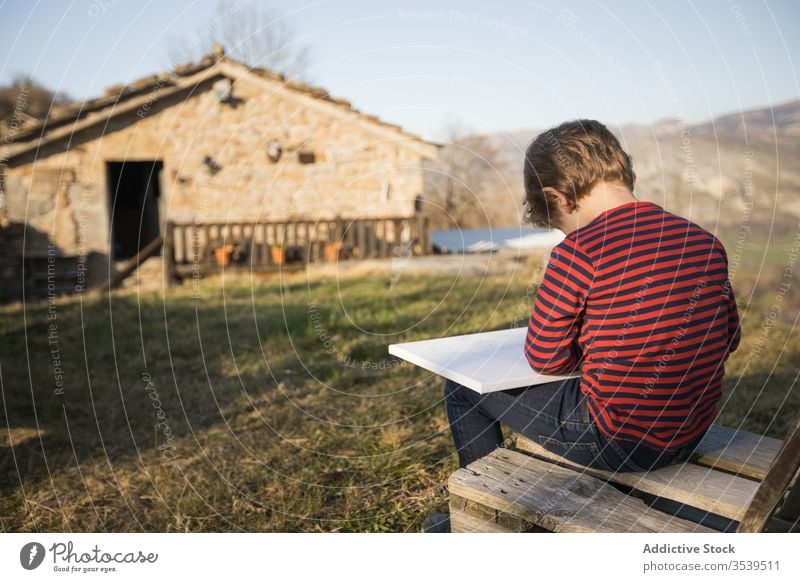 Junge zeichnet, während er auf einer Bank in einem Dorf im Hochland sitzt zeichnen Leinwand Inspiration Kunst Farbe Berge u. Gebirge Hobby Kind Landschaft