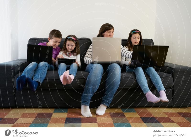 Seriöse Mutter und Kinder verbringen zu Hause Zeit miteinander, indem sie Gadgets auf dem Sofa benutzen Laptop beschäftigt Süchtige benutzend heimwärts