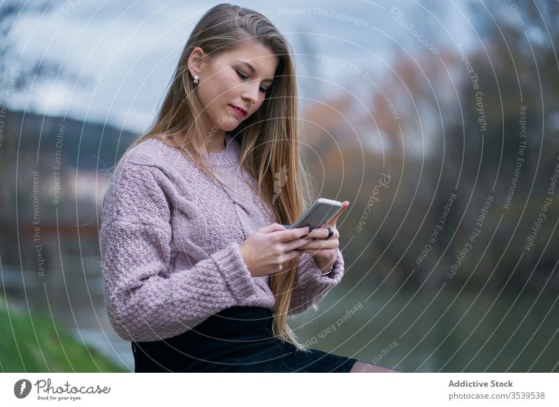 Lächelnde Frau surft auf einem Smartphone, während sie sich bei Sonnenuntergang im Park ausruht Browsen ruhen Glück heiter froh benutzend zuschauend