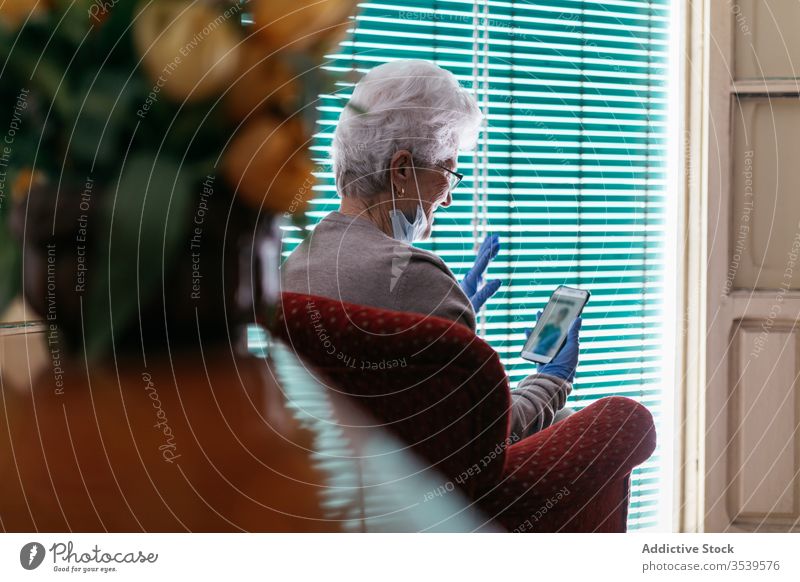 Alte Frau bei Videogesprächen auf Smartphone zu Hause Aufenthalt heimwärts Coronavirus Senior Videoanruf benutzend heiter Kommunizieren gestikulieren Gruß