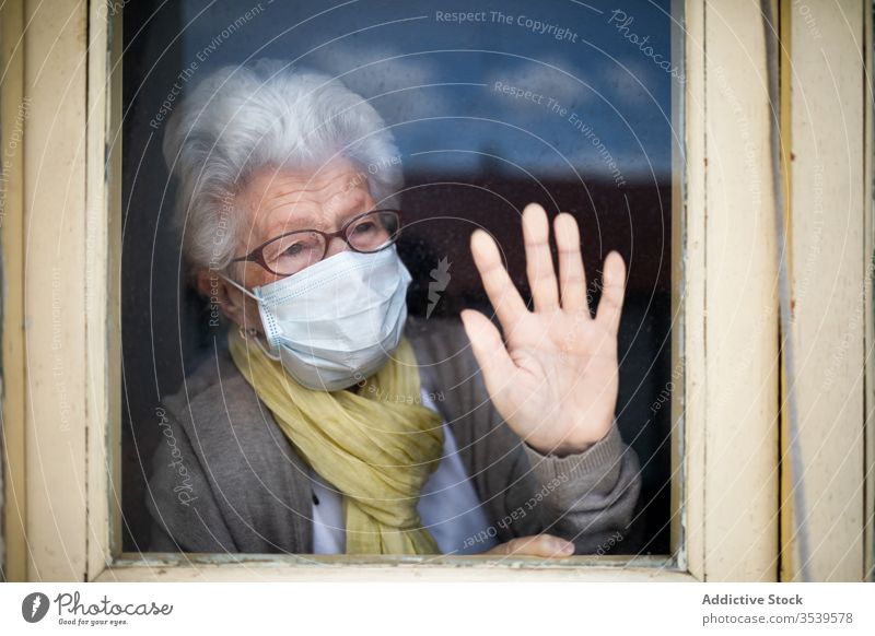 Ältere Frau mit Schutzmaske, die aus dem Fenster schaut Senior Coronavirus Mundschutz heimwärts einsam Anspannung verzweifelt unglücklich traurig Quarantäne