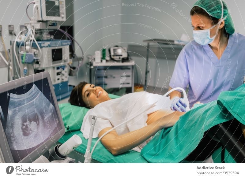 Gynäkologe untersucht Patientin während der Ultraschalluntersuchung in der Klinik Frauenarzt Ultraschall-Scan geduldig schwanger Monitor Embryo Mundschutz