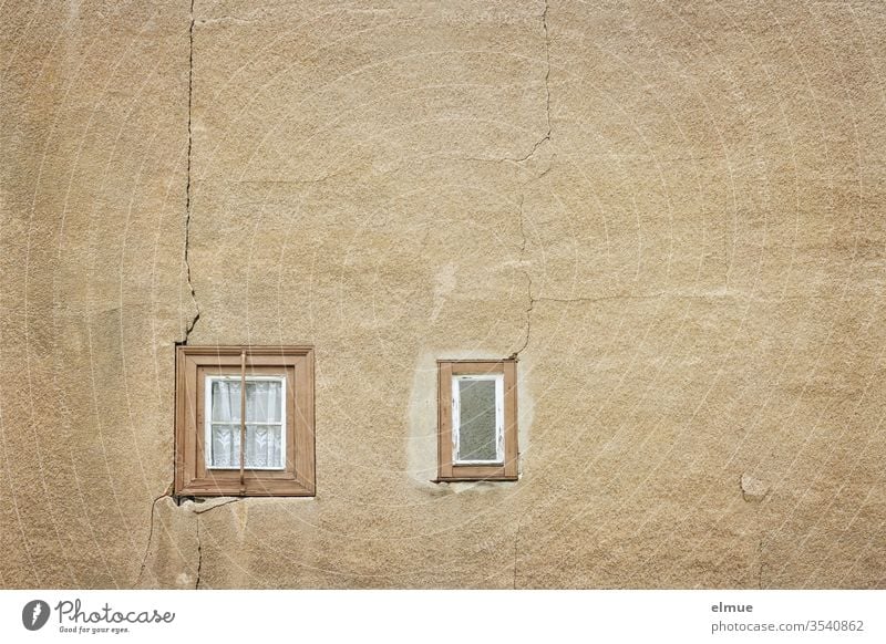 zwei winzige, ganze Holzfenster in einer sandfarbenen Wand mit Rissen Fenster marode Gardine Verfall Spekulationsobjekt Ausblick baufällig Altbauwohnung Putz