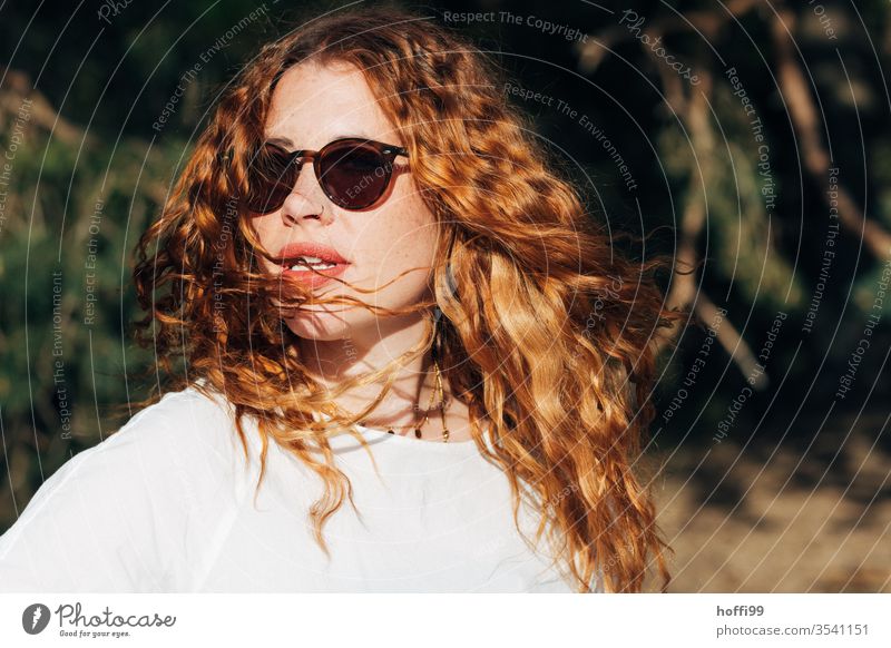 junge Frau mit Sonnenbrille und roten lockigen Haaren dreht sich der Sonne entgegen rote Haare rote lippen Locken lockiges haar rothaarig rote Lippen schön