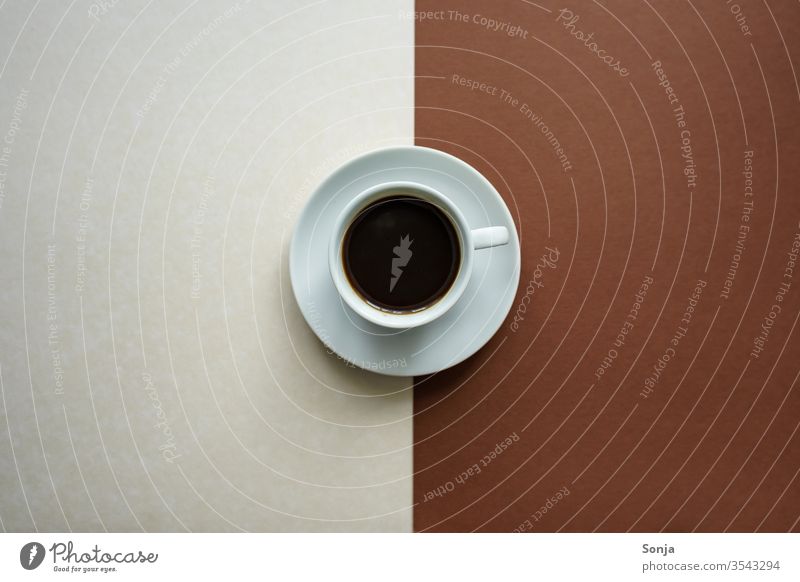 Eine weiße Tasse mit Kaffee und eine Untertasse auf einem weißen und braunen Hintergrund, Gegensätze Getränk Espresso schwarz stark aromatisch heiß Gegensatz