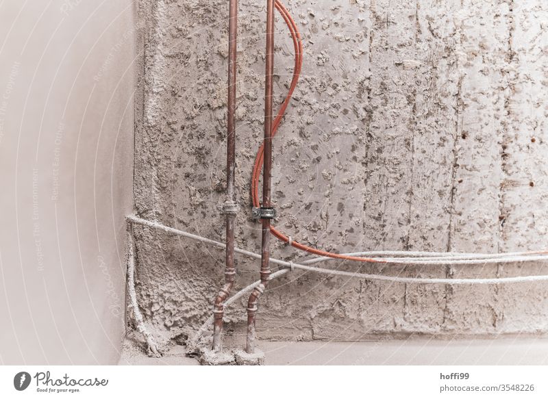 Wasserleitung, Rohrleitung und Kabel  im Rohbau Putzfassade Montage Wand Baustelle Fassade Mauer graue Wand Metall Stahlkabel Leitung Wasserrohr verbinden
