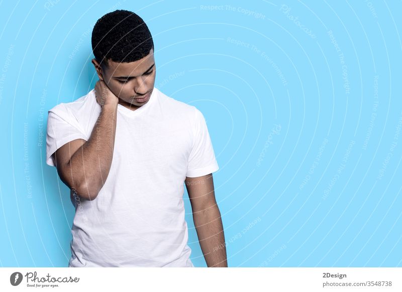 Nahaufnahme eines jungen schwarzen Mannes isoliert auf blauem Hintergrund in lässigem weißem T-Shirt, den Hals berührend, mit den Fingern nachdenklich und besorgt nach unten blickend