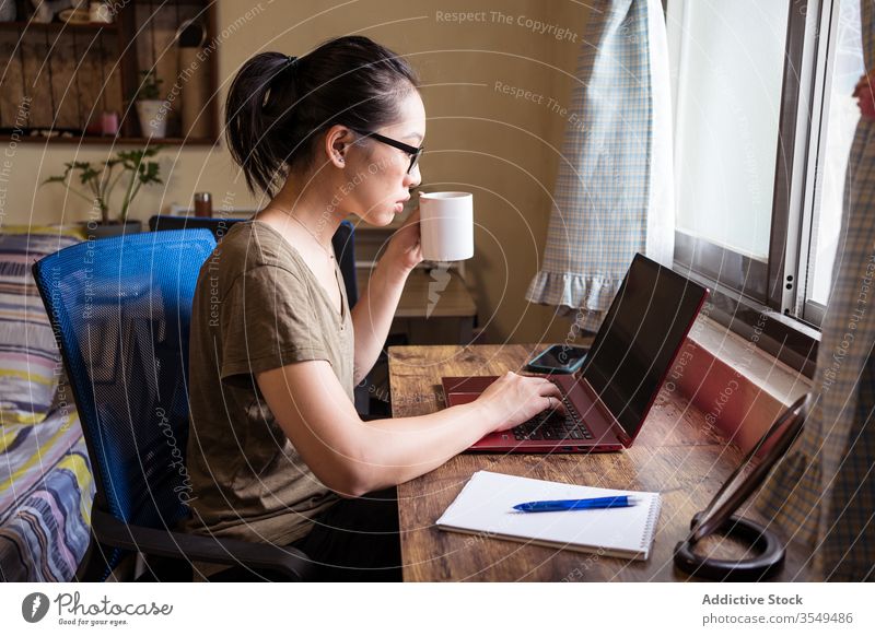 Vielbeschäftigte Unternehmerin tippt am Laptop und trinkt Kaffee Tippen Frau trinken heimwärts Büro benutzend asiatisch ethnisch freiberuflich Konzentration