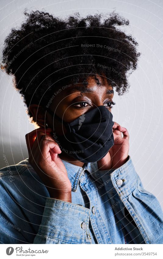 Junge schwarze Frau mit Schutzmaske Mundschutz Coronavirus zu Hause bleiben COVID jung Afroamerikaner ethnisch Afro-Look lässig behüten Sicherheit abstützen