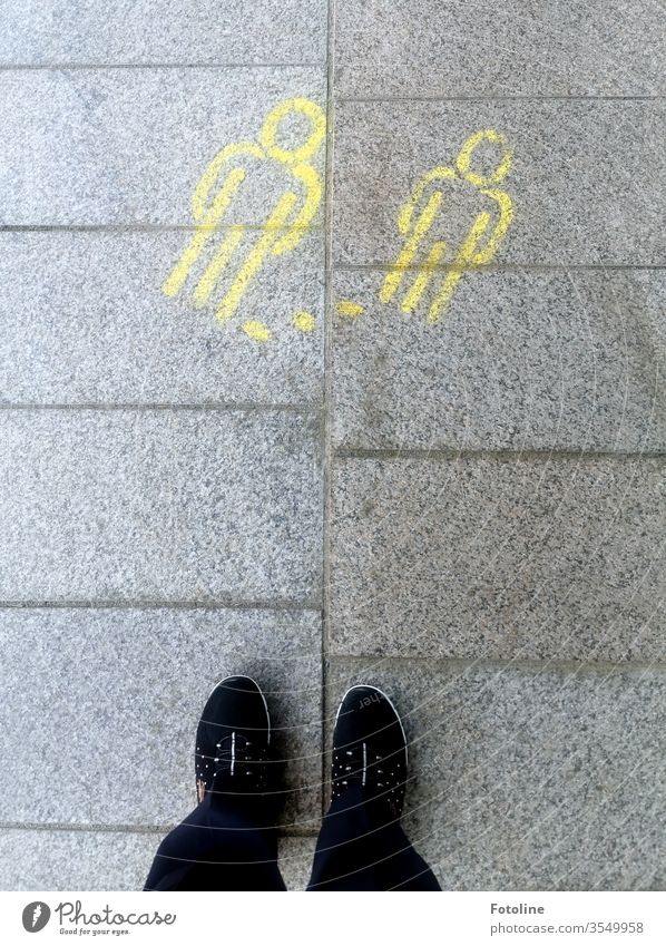 Abstand halten! - oder zwei gelbe Strichmännchen, die auf den Boden gemalt sind, weisen auf die Abstandsregel hin Schuhe Fuß Mensch stehen Außenaufnahme