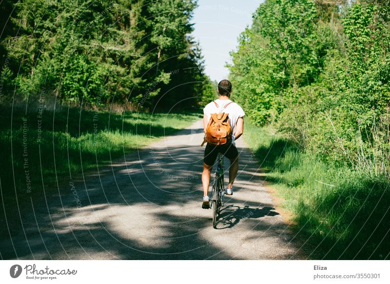 Ein Radfahrer auf einem Weg durch den Wald auf einem Ausflug mit dem Fahrrad Fahrradfahrer Mann Natur Fahrradtour Sommer sonnig Rucksack T-Shirt dunkelhaarig