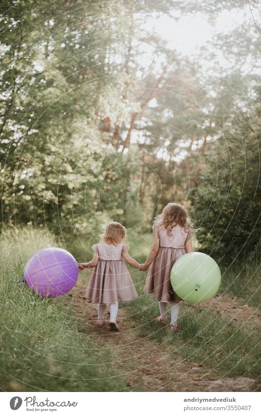 zwei hübsche kleine Mädchen im Sommer in einem Park mit Luftballons in der Hand. Glückliches Mädchen mit Luftballons. Kinder Ballons Freiheit Familie Spielen