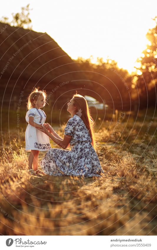 Glückliche und liebevolle Familie in der Natur. Emotionale und fröhliche junge blonde Mutter mit ihrer kleinen lachenden kleinen Tochter, die den Regenbogen sitzend betrachtet. Sommerlicher Spaß.