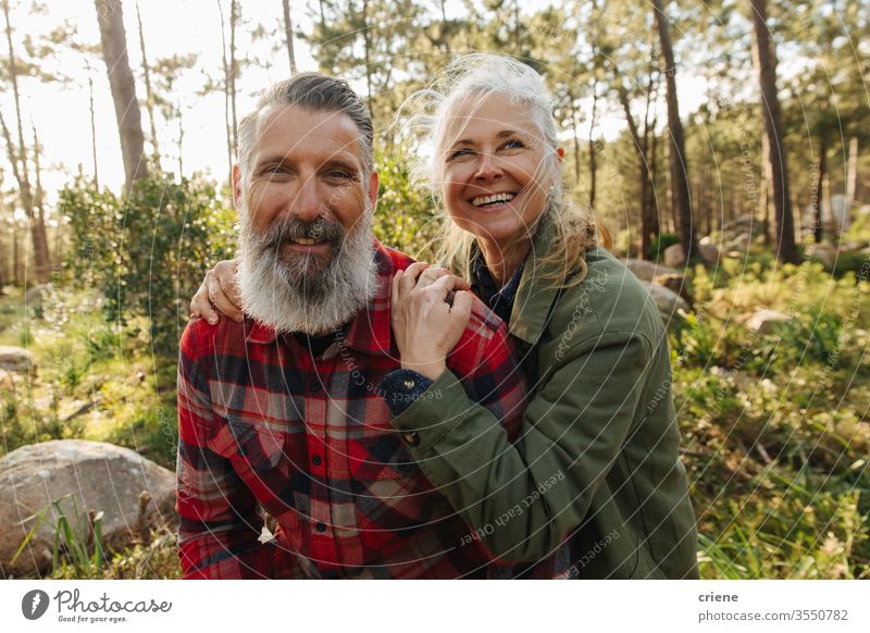 Porträt eines glücklich lächelnden älteren Paares auf einer Wanderung im Wald in die Kamera schauen sonnig Lachen offen Familie Reisende Sport Kaukasier Wälder