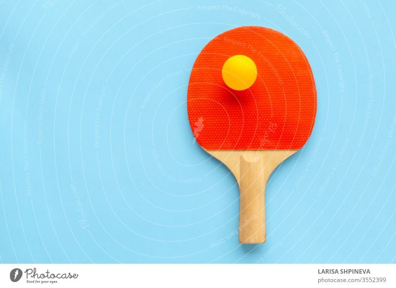 Roter Schläger für Tischtennis mit gelbem Ball auf blauem Hintergrund. Tischtennis-Sportgerät in minimalem Stil. Flachlegung, Draufsicht, Kopierraum pong Ping