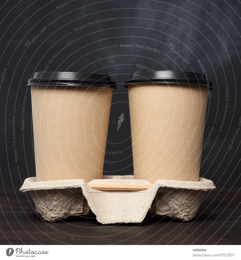 zwei braune Einwegbecher aus Papier mit Kunststoffdeckel stehen in der Schale auf einem Holztisch Container Deckung Tasse Einwegartikel trinken leer americano
