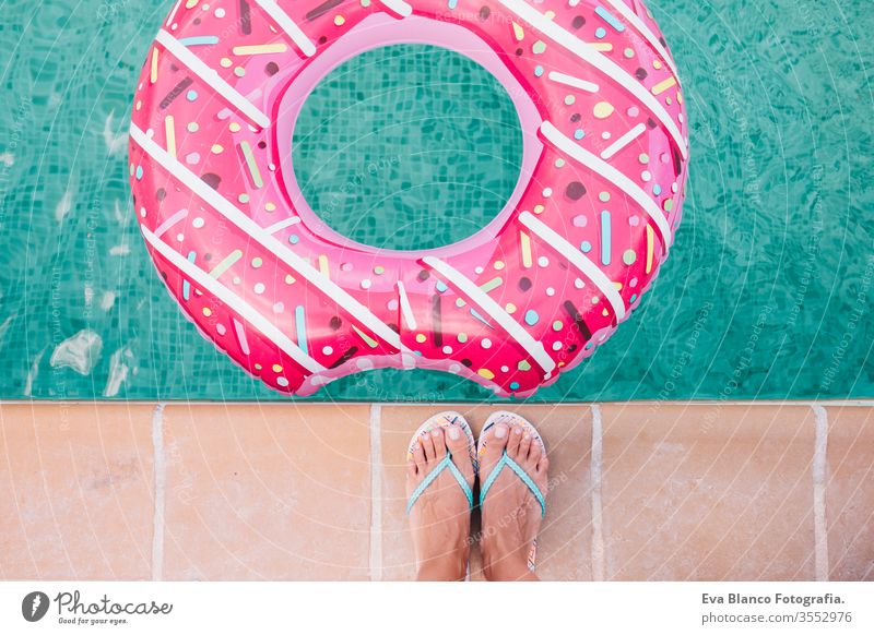 Draufsicht auf die Füße einer Frau im Liegen. Frau entspannt sich im Pool mit rosa Donuts an einem heißen sonnigen Tag. Sommerurlaub idyllisch. Sonnenbräune genießen Frau im Bikini auf der Hüpfburg im Schwimmbad.