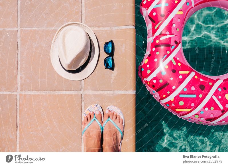 Draufsicht auf eine flach auf den Füßen liegende Frau mit Hut und Sonnenbrille. Frau entspannt sich im Pool mit rosa Donuts an einem heißen sonnigen Tag. Sommerurlaub idyllisch. Urlaubskonzept