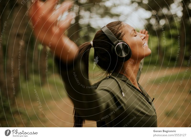 Junge Frau mit Kopfhörern, die ihre Arme im Wald vorhalten, weil sie gerne draußen trainiert Musik hören Lifestyle Kaukasier Fröhlichkeit im Freien Athlet Natur