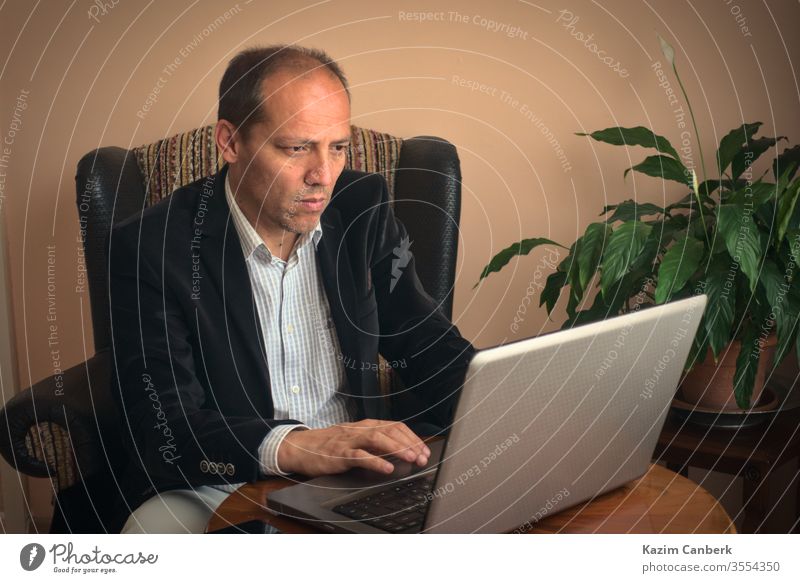 Älterer erwachsener Mann, der von zu Hause aus mit seinem Laptop mit Pflanze im Hintergrund arbeitet Arbeit von zu Hause aus älterer Mann Telearbeit heimwärts