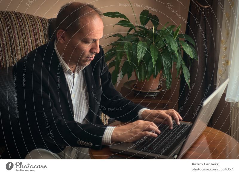 Schwerer männlicher Erwachsener, der von zu Hause aus arbeitet und am Laptop mit einer Pflanze auf dem Hintergrund tippt Arbeit von zu Hause aus älterer Mann