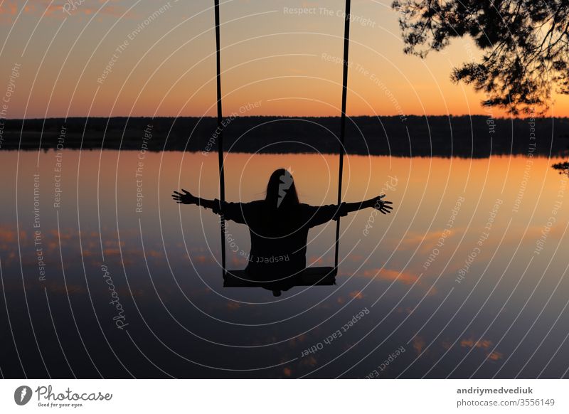 romantische junge Frau auf einer Schaukel über dem See bei Sonnenuntergang. Junges reisendes Mädchen auf der Schaukel sitzend in schöner Natur, Blick auf den See