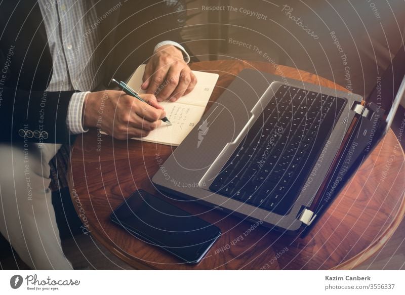 Älterer Mann macht Notizen mit Stift, während er mit seinem Laptop eine Telefonkonferenz führt Arbeit von zu Hause aus mitschreibend Hände Computer männlich