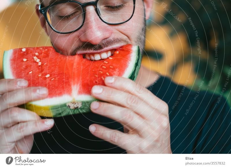 Ein Mann beißt in ein Stück Wassermelone reinbeißen Biss lecker essen lächeln gesund fruchtig Freude schlemmen Frucht saftig naschen Ernährung rot Gesundheit