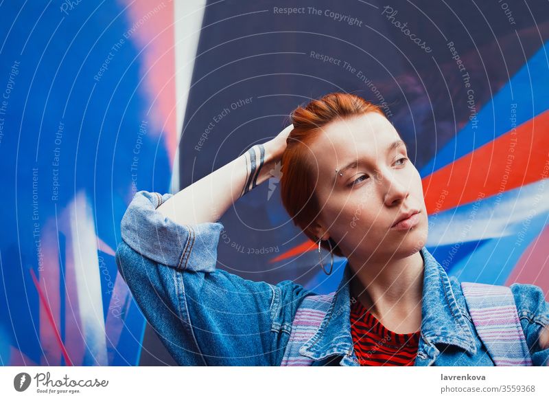 Junge erwachsene weiße Frau in Jeansjacke mit abgestorbenen roten Haaren flacht ihr Haar ab, Lifestyle-Porträt mit selektivem Fokus Jacke Jeanshose Model Straße