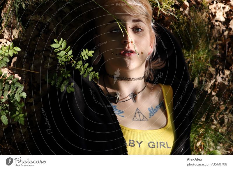Portrait einer jungen Frau mit Piercings, Tätowierungen und Tunnel, die auf dem Waldboden liegt Mädchen blond Schmuck Assecoires Shirt Hemd schön draussen